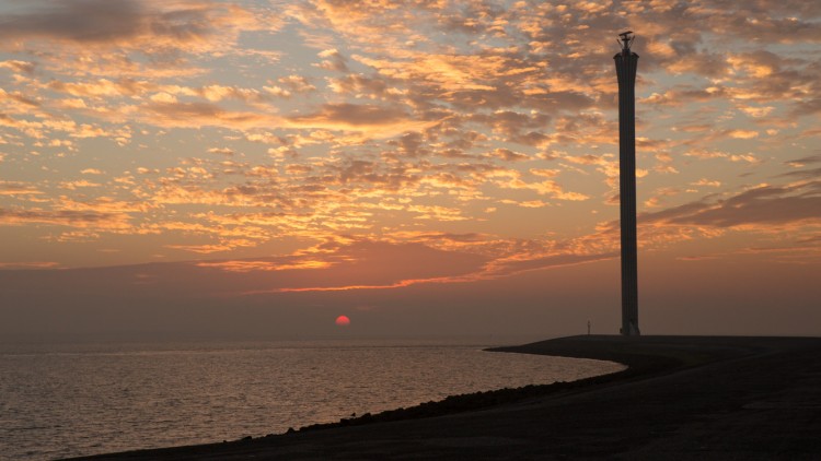 Foto van de ondergaande zon en een radartoren aan de Schelde.