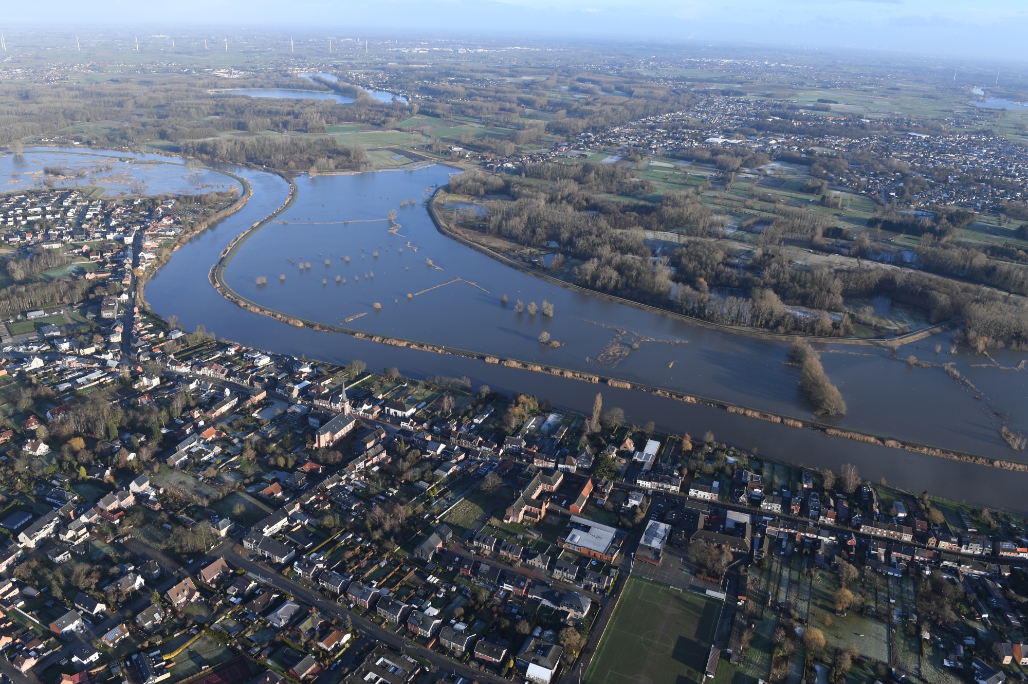 Overzichtsfoto van een overstroomd natuurgebied naar de rivier. Aan de andere kant van de rivier staan woningen.