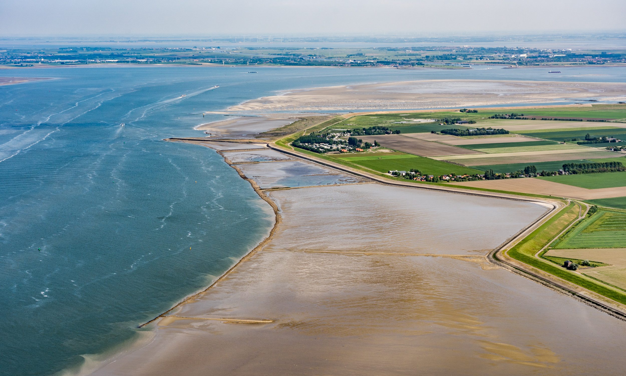 Luchtfoto met water, zand, een kustlijn en platteland.