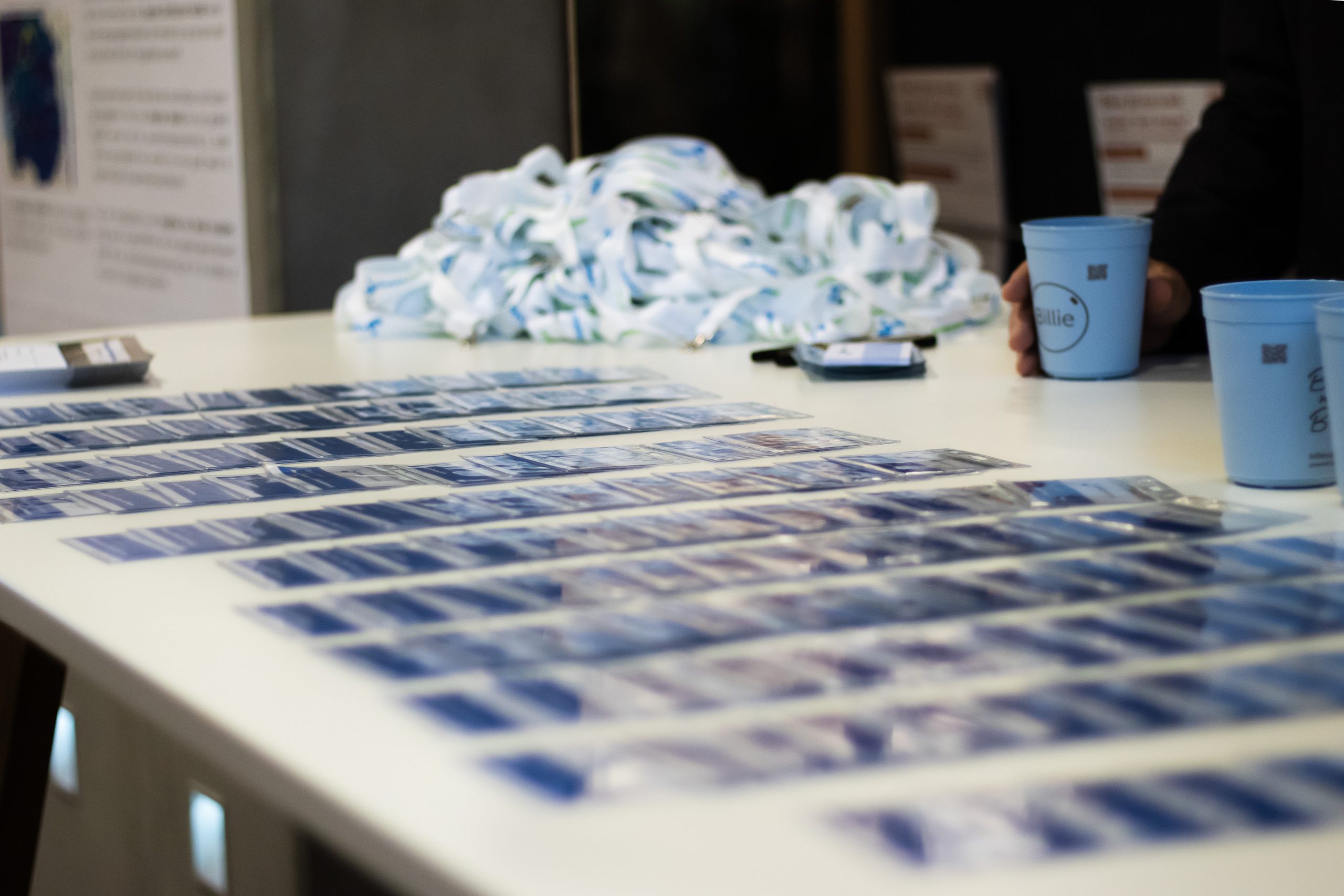 Foto van blauwe badges klaargelegd op een tafel. Op de achtergrond zijn de witte keycords zichtbaar.