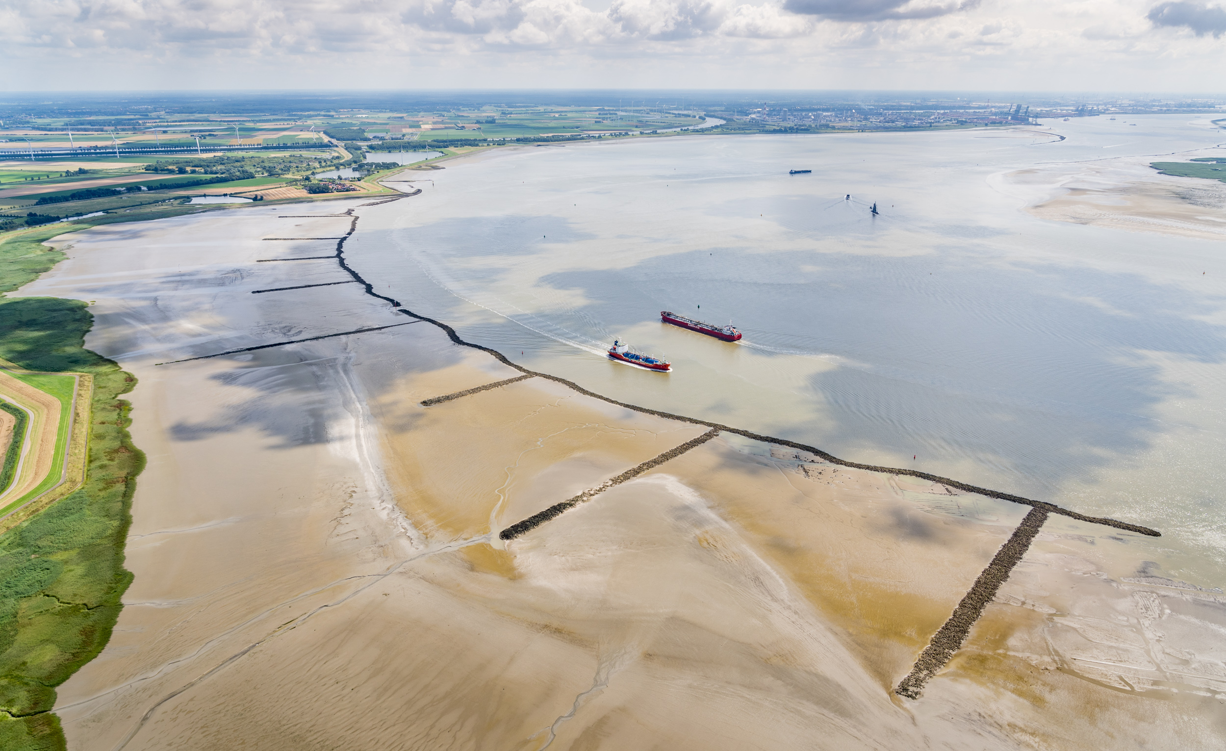 Luchtfoto van de Westerschelde met strekdammen op de voorgrond